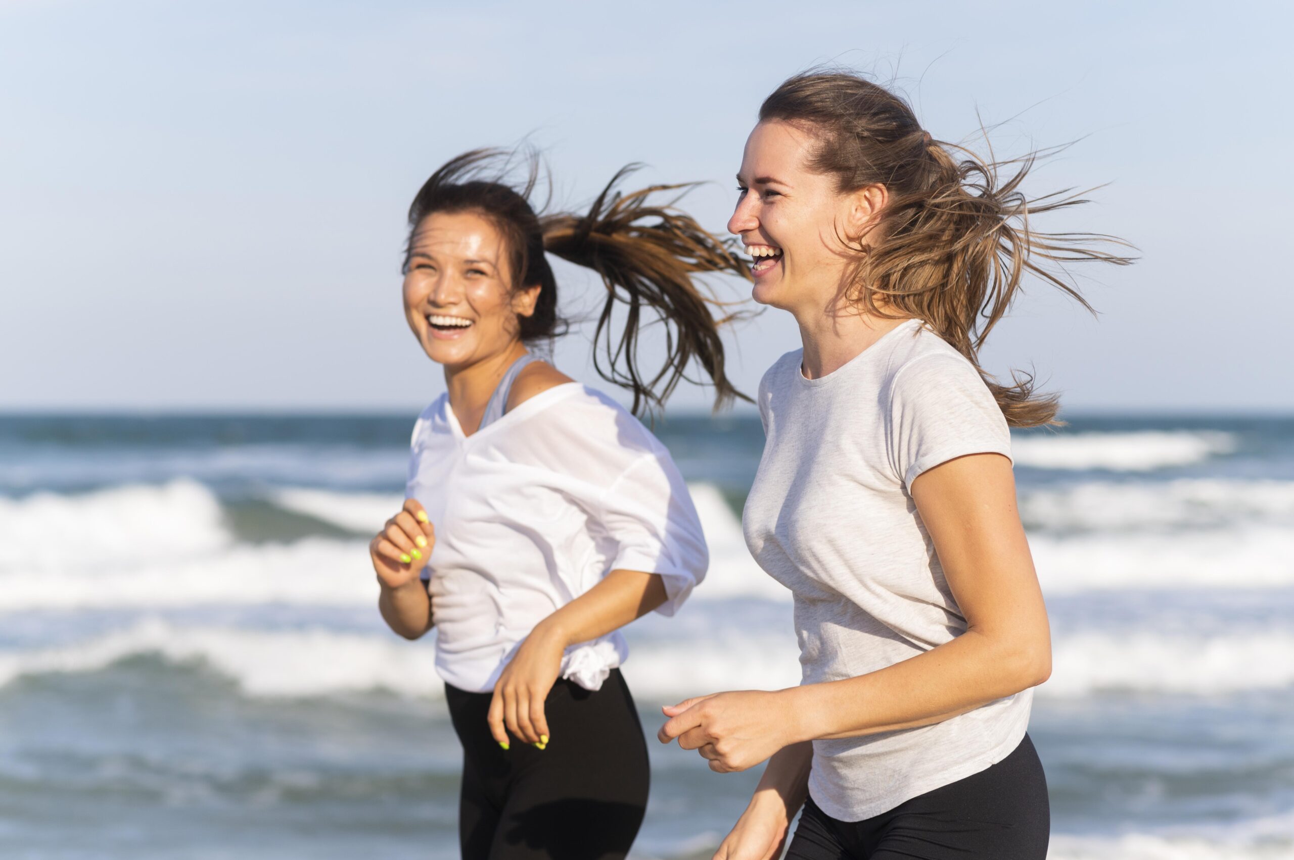side view smiley women running together beach side view smiley women running together beach